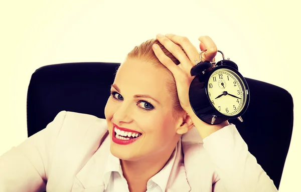 책상 뒤에 앉아 및 알람 시계를 들고 행복 한 비즈니스 우먼 — 스톡 사진