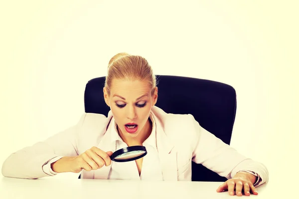 Donna d'affari seduta dietro la scrivania e guardando in una lente d'ingrandimento — Foto Stock