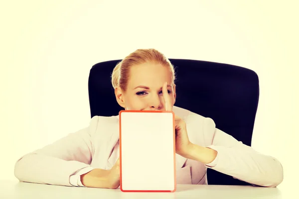 Young business woman sitting behind the desk and holding a board with ban — Stock Photo, Image