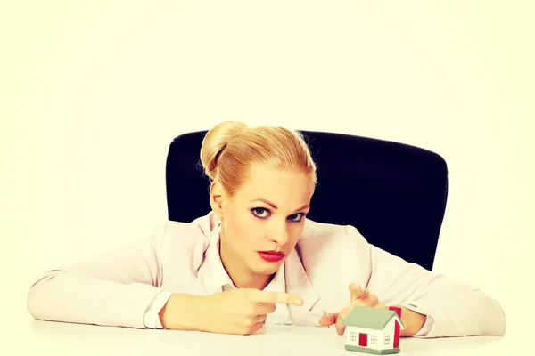 Business woman sitting behind the desk and pointing for house model — Stock Photo, Image