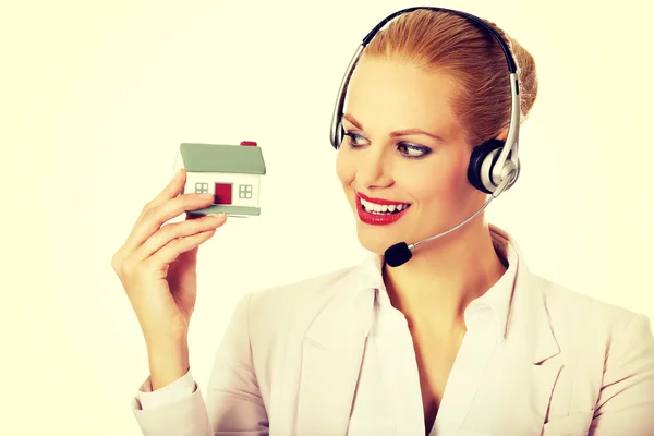 Joven mujer de negocios en auriculares sosteniendo modelo de casa —  Fotos de Stock