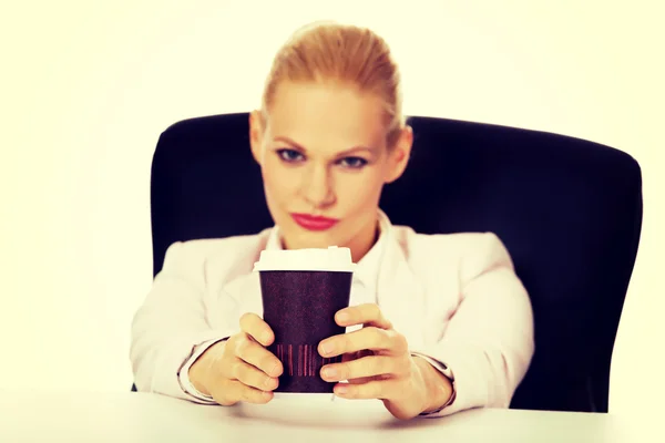 Zakenvrouw met koffie in papier beker zitten achter de desk — Stockfoto