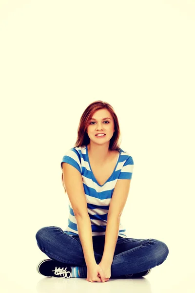 Mulher adolescente sorridente sentada em um chão com as pernas cruzadas — Fotografia de Stock