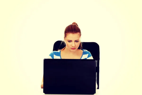 Teenage angry woman with laptop sitting behind the desk — Stock Photo, Image