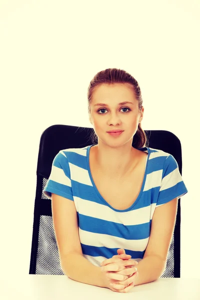 Mujer adolescente sonriente sentada detrás del escritorio — Foto de Stock