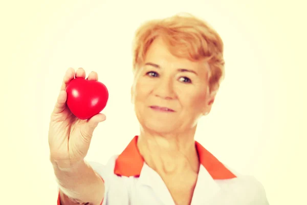 Uśmiech starszych kobiet lekarz lub pielęgniarka trzymając czerwony zabawka serca — Zdjęcie stockowe