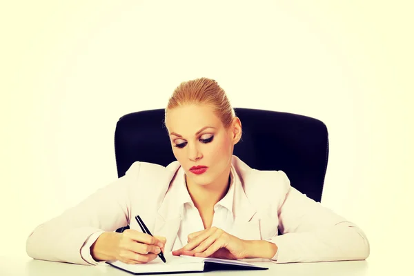 Zamyślony biznes kobieta robi notatki za biurkiem — Zdjęcie stockowe