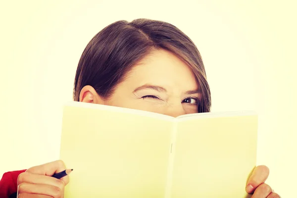 Woman hiding her face behind a notebook. — Stock Photo, Image