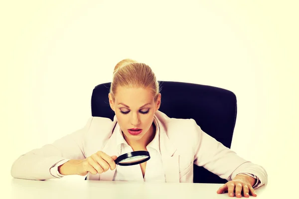 Zakelijke vrouw zit achter het bureau en kijkt in een vergrootglas — Stockfoto