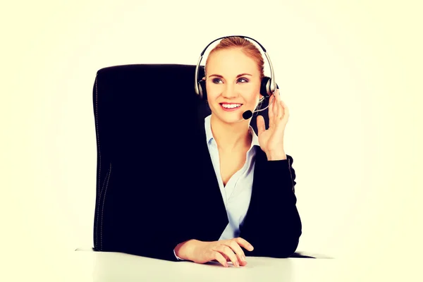 Uśmiechnięty operator telefonu w słuchawkach siedzący za biurkiem — Zdjęcie stockowe