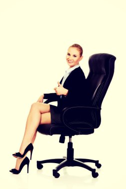 Genç gülümseyen iş kadını ofiste bir sandalyede oturuyor.