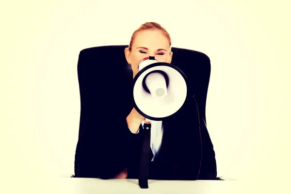 Mulher de negócios sentada atrás da mesa e gritando através de um megafone — Fotografia de Stock