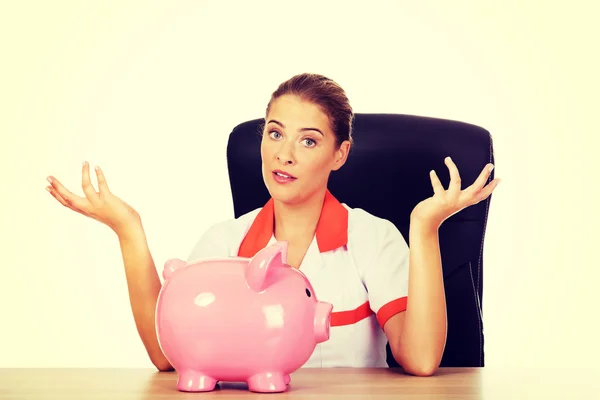 Female doctor  sitting behind the desk and holding a piggybank — Stock Photo, Image