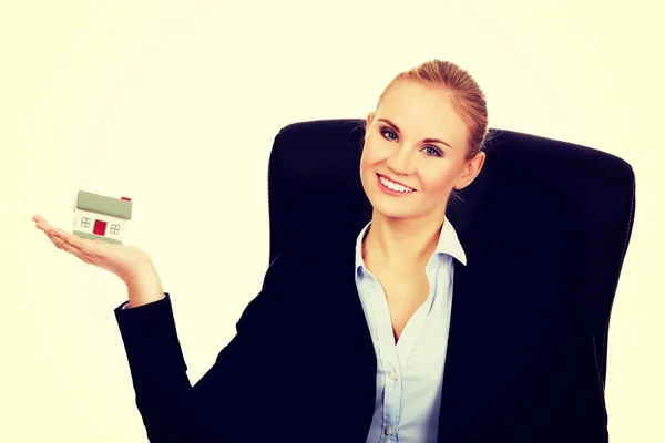 Smiling business woman sitting on a chair and holding house model — Stock Photo, Image