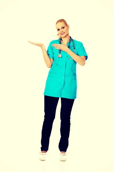 Kvinnliga läkare eller sjuksköterska presentera copyspace eller något på öppen handflata och pekar för detta leende — Stockfoto