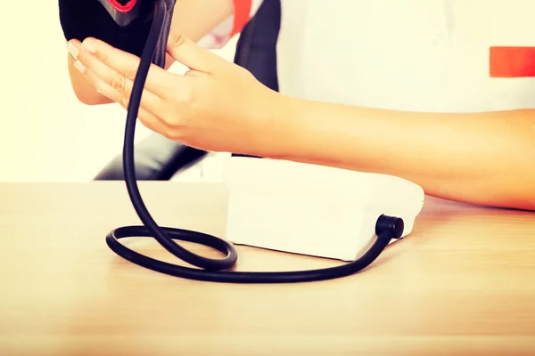 Läkare som sitter bakom skrivbordet håller blodet manometer — Stockfoto