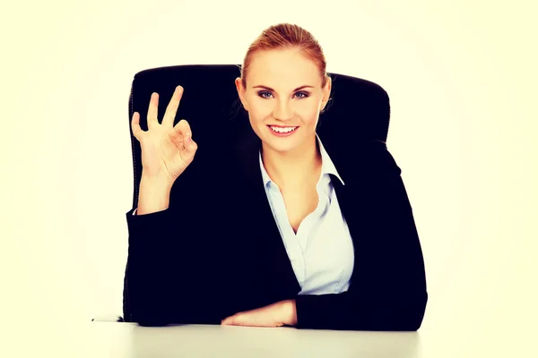 Mujer de negocios feliz sentado detrás del escritorio y muestra signo OK — Foto de Stock