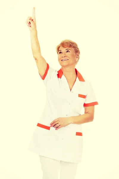 Smile elderly female doctor or nurse pointing up — Stock Photo, Image