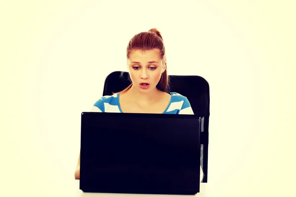 Adolescente chocado mulher com laptop sentado atrás da mesa — Fotografia de Stock