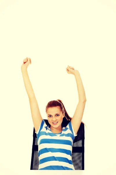 Teenage woman sitting behind the desk with arms up — Stock Photo, Image