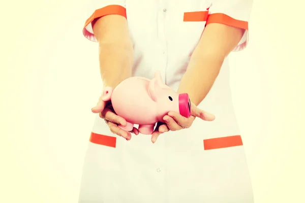 Smile elderly female doctor or nurse holding piggybank — Stock Photo, Image
