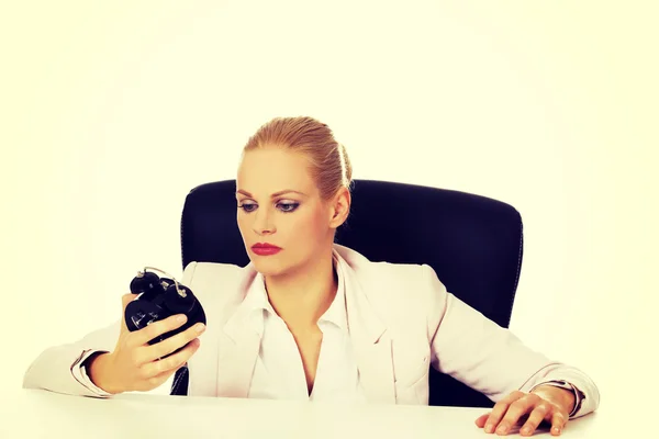 Mujer de negocios cansada sentada detrás del escritorio y sosteniendo el despertador —  Fotos de Stock