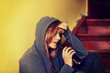 Genç bunalımlı kadın merdivenlerde oturuyor ve bira içiyor.