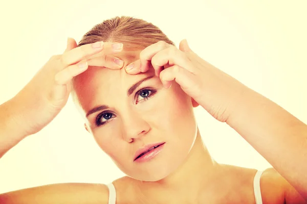 Unhappy young woman squeezing pimple on face — Stock Photo, Image