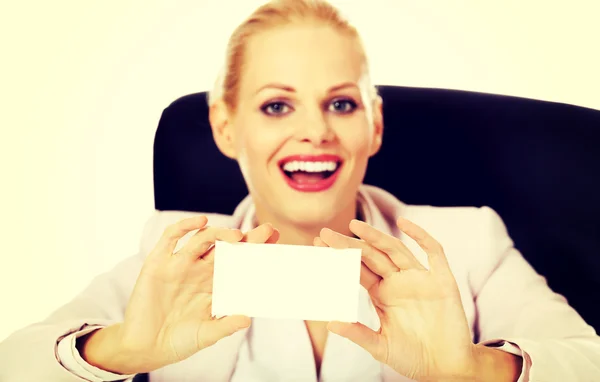 Sonríe mujer de negocios sentada detrás del escritorio y sosteniendo la tarjeta de bullicio vacía —  Fotos de Stock