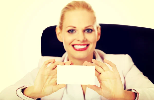 Sonríe mujer de negocios sentada detrás del escritorio y sosteniendo la tarjeta de bullicio vacía —  Fotos de Stock
