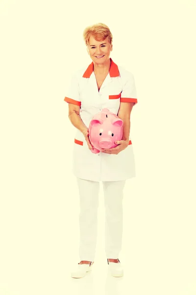 Sorria idosa médica ou enfermeira segurando piggybank — Fotografia de Stock