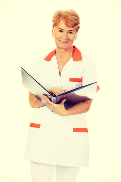 Elderly female doctor or nurse holds black binder and reads — Stock Photo, Image