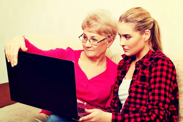 Dcera a matka sedí na gauči a sledovat něco na laptop — Stock fotografie
