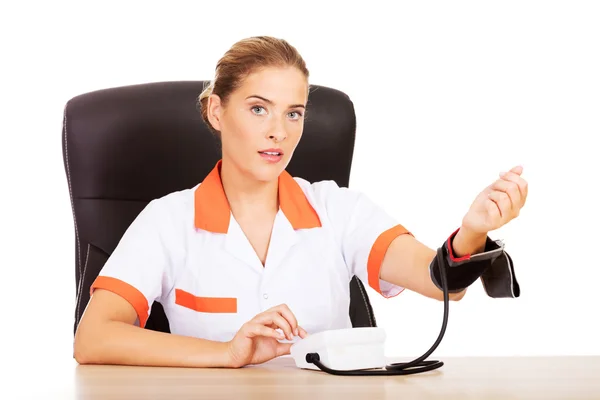 Lekarz siedzi za biurkiem gospodarstwa miernika ciśnienia krwi — Zdjęcie stockowe