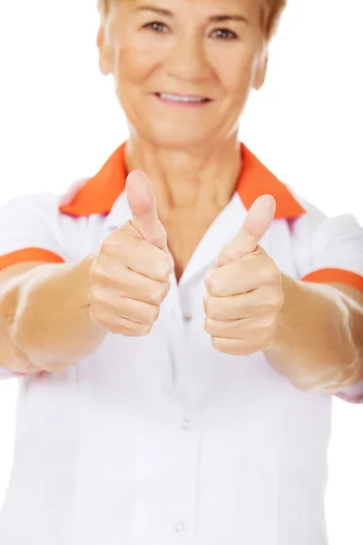 Улыбающаяся пожилая женщина-врач или медсестра показывает большие пальцы вверх — стоковое фото