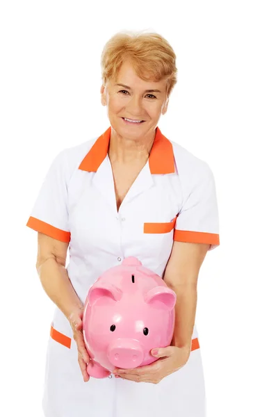 Idős női orvos vagy a nővér gazdaság piggybank mosoly — Stock Fotó