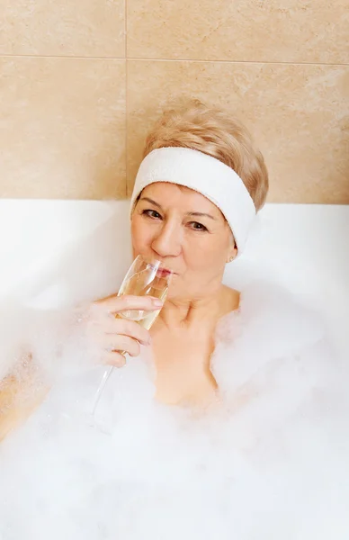 Ανώτερος γυναίκα χαλαρώνοντας στο μπάνιο με ποτήρι σαμπάνιας — Φωτογραφία Αρχείου