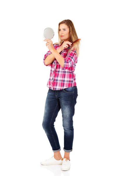 Junge Frau hält Spiegel und kämmt sich die Haare — Stockfoto