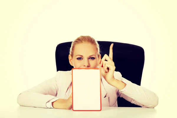 Joven mujer de negocios sentada detrás del escritorio y sosteniendo una tabla con prohibición — Foto de Stock