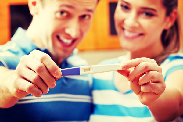 Young happy couple with pregnancy test standing in kitchen