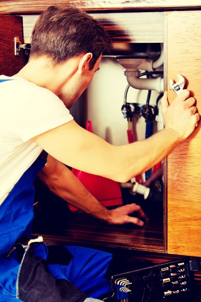 Joven reparar algo dentro del gabinete de la cocina debajo del fregadero — Foto de Stock