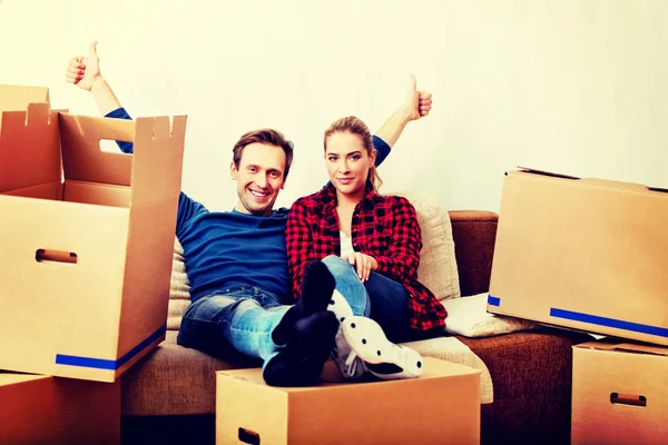 Pasangan bahagia yang lelah duduk di sofa di rumah baru dengan kotak-kotak papan tulis di sekitarnya — Stok Foto