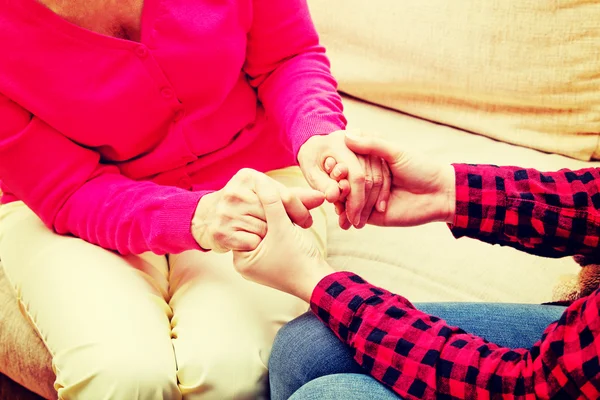 Mother and daughter sitting on couch and holding hands — Stock Photo, Image