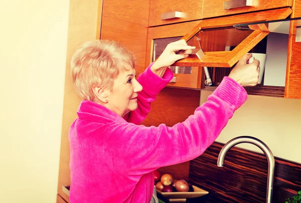 Gülümsemek üst düzey kadın kupa bir mutfak kabine alarak — Stok fotoğraf