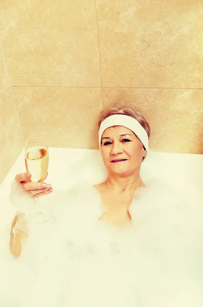 Senior woman relaxing in bath with glass of champagne — Stock Photo, Image