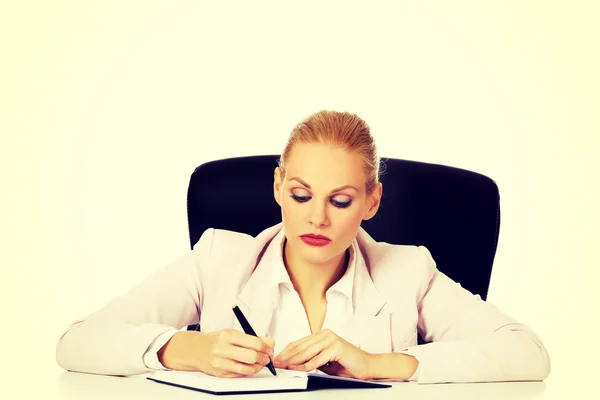 Pensive zakenvrouw neemt notities achter het bureau — Stockfoto