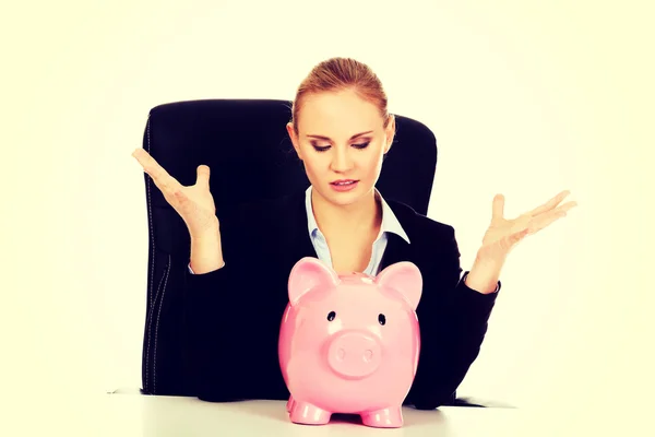 Worried business woman with a piggybank behind the desk — Stock Photo, Image
