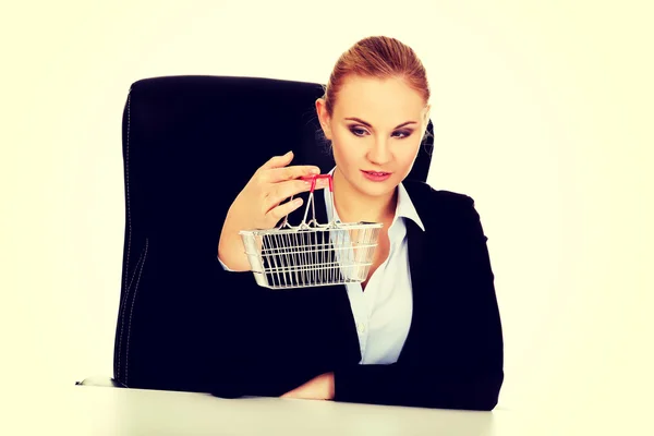 Smile business woman holding shopping cart and sitting behind the desk — Stock Photo, Image