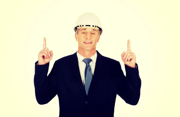 Hombre de negocios sonriente con el sombrero duro apuntando hacia arriba —  Fotos de Stock