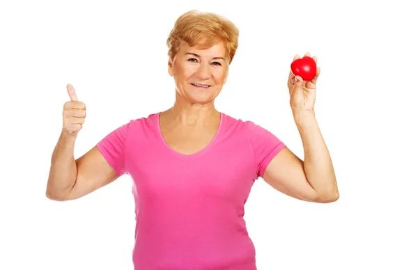 Viejo sonriente mujer sosteniendo rojo juguete corazón con pulgar hacia arriba —  Fotos de Stock